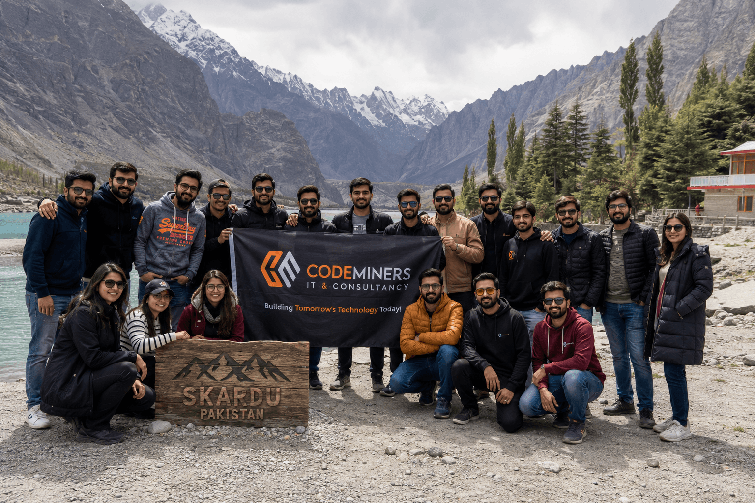 The complete CodeMiners engineering team at Skardu, Pakistan — annual company retreat with the entire 150-person team holding CodeMiners banner against Karakoram mountain range and Attabad Lake